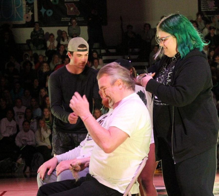 As sophomore Salem Sobocinski cuts his hair, math teacher John Gilbert winces while senior Anthony Valenti shaves science teacher James O’Daniel’s head (not pictured). Both teachers auctioned the chance to cut their hair at the assembly in support of St. Baldricks.