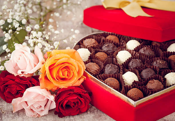 A box of Valentine's chocolates, paired with a bouquet of pink, red, and orange flowers.