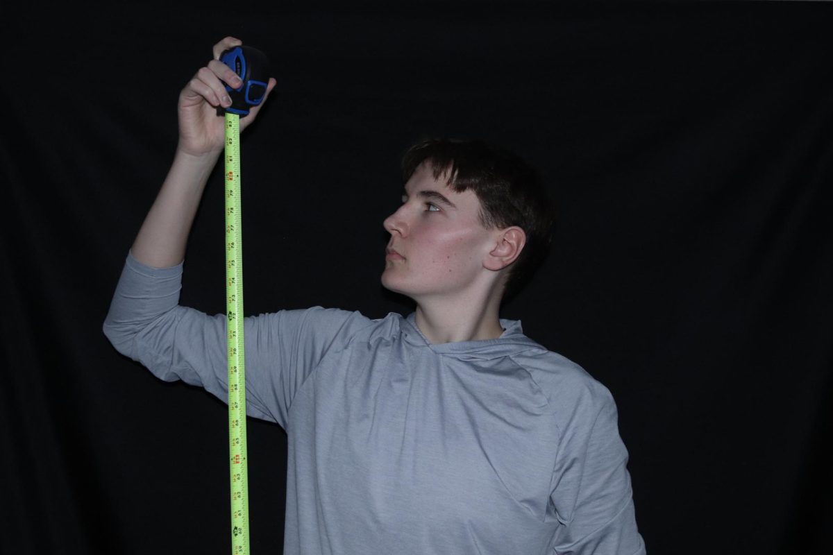 Senior Patrick Sabinson is photographed measuring his height with a measuring tape.