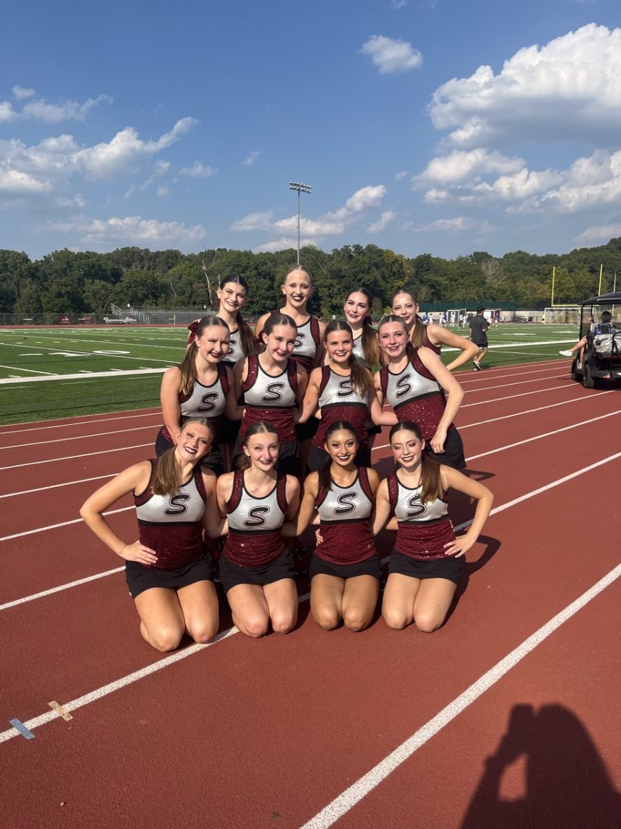 From left to right, back to front, freshmen Natalie Niewoehner, Cece Blinkinsop, Emerie Hutzler, sophomore Alissa Tranchilla, freshmen Taylor Springer, Gracie, Kyle, Laney Carron, Caylie Markotay, Hailey Fister, Haleigh Grefemkamp, Raaga Tota, and Addison Porte, pose together on the sideline of the football field. (photo by Rachel Rea)