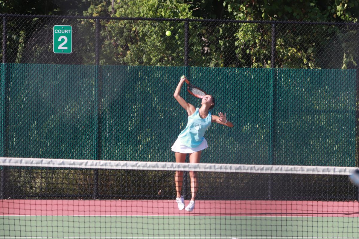 Jumping to hit the ball, senior Isabel Duan serves over the net.