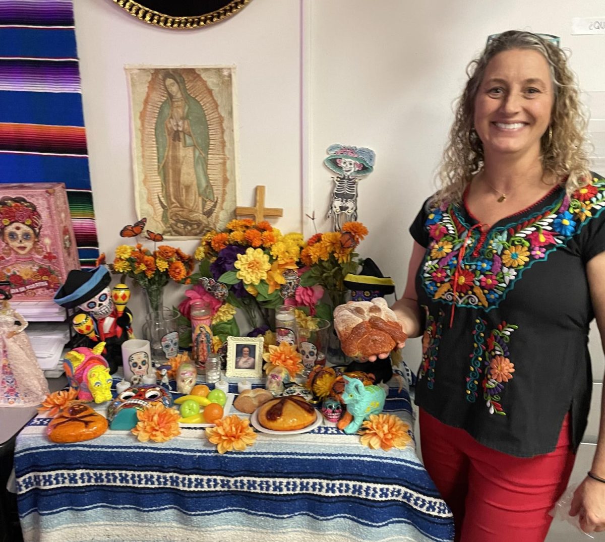 Holding a loaf of Pan de Muerto, Spanish teacher Cady Villmer poses by her ofrenda. Villmer created this ofrenda for Dia de Los Muertos last year. It features marigolds, candles, a cross, sugar skulls, and a photo of her grandma.(photo used with permission by Cady
Villmer)