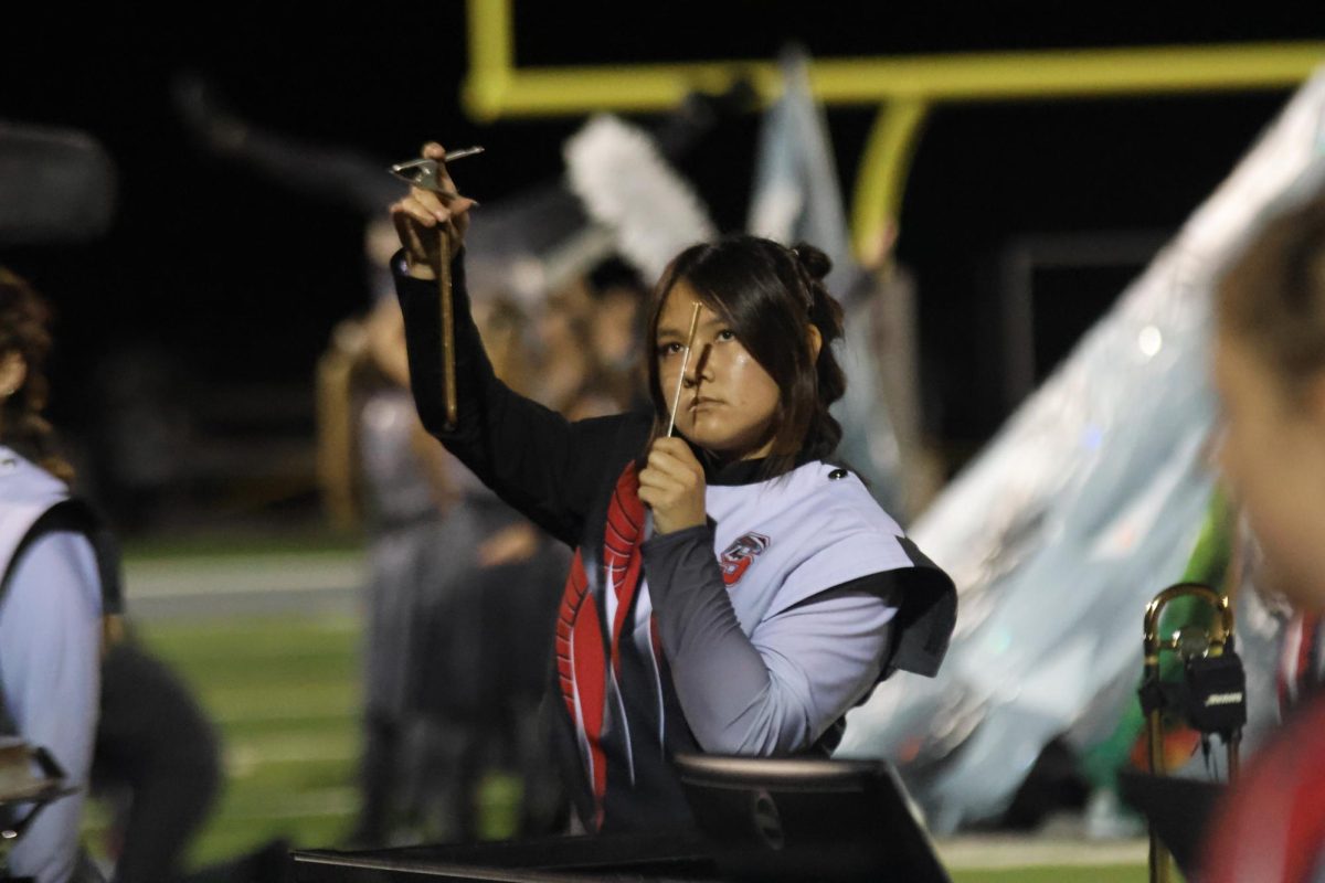 Holding up a triangle, sophomore Olivia Hirata watches for the right moment to strike the instrument. The marching band performed their show "Luxe" at the football game on Oct. 24.