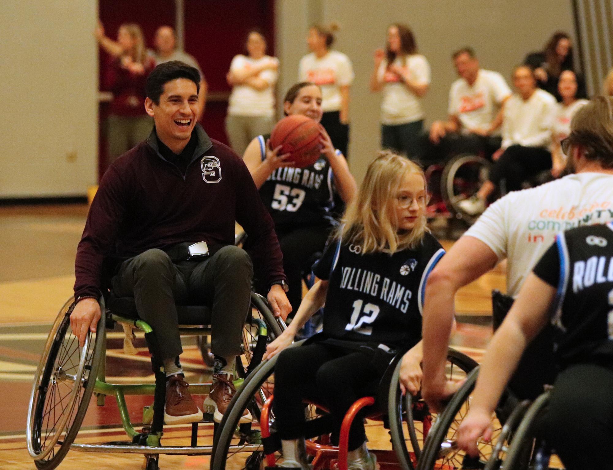 Rolling down the court, sophomore principal Dr. Joshua Flores smiles at Addie Pardeck (12) while playing in the wheelchair basketball game.
